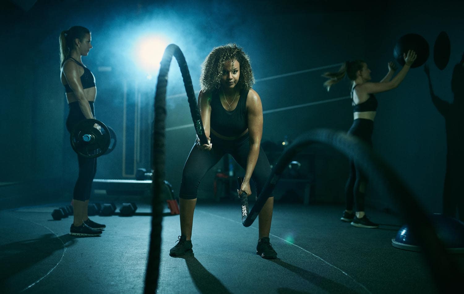 Female athlete in the gym doing renegade rows with dumbells. Dark and moody feel