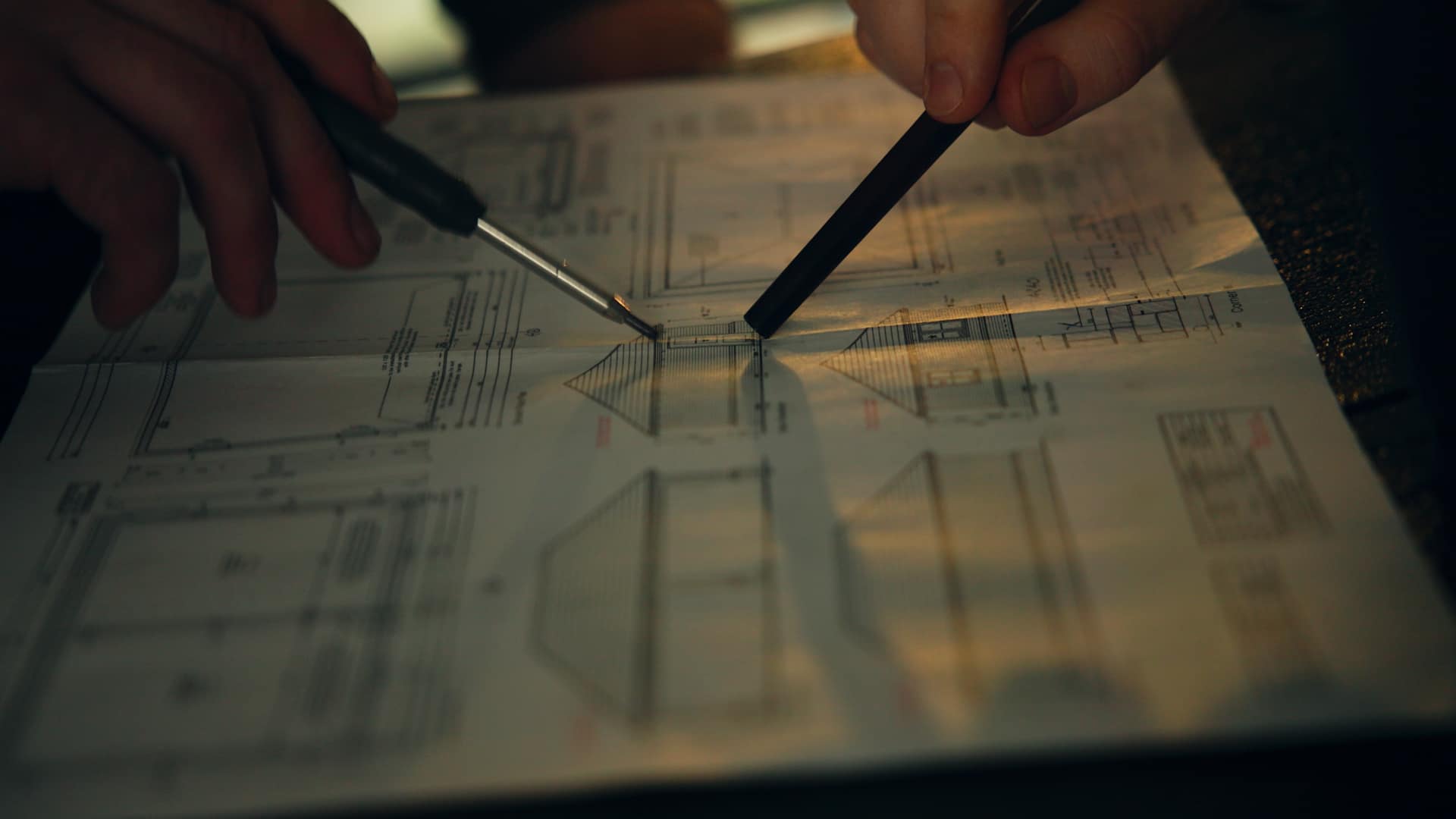 Close up of two workers looking over plans. Only their hands and pens can be seen pointing out parts of the plans