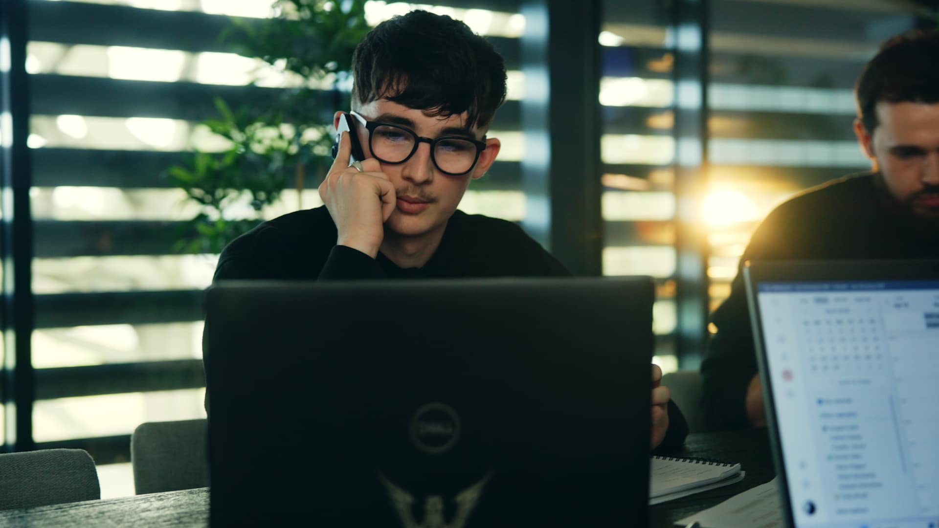 An office working on the phone while looking at his laptop