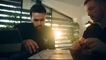 Two men backlit at a desk looking over plans