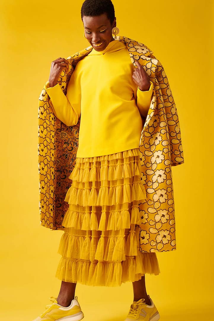 A model wearing a layered yellow outfit on a yellow background